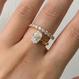 May include: Two gold rings with diamonds. The first ring has a large oval-cut diamond as the centerpiece. The second ring is a gold band with a row of smaller diamonds. The rings are on a finger.