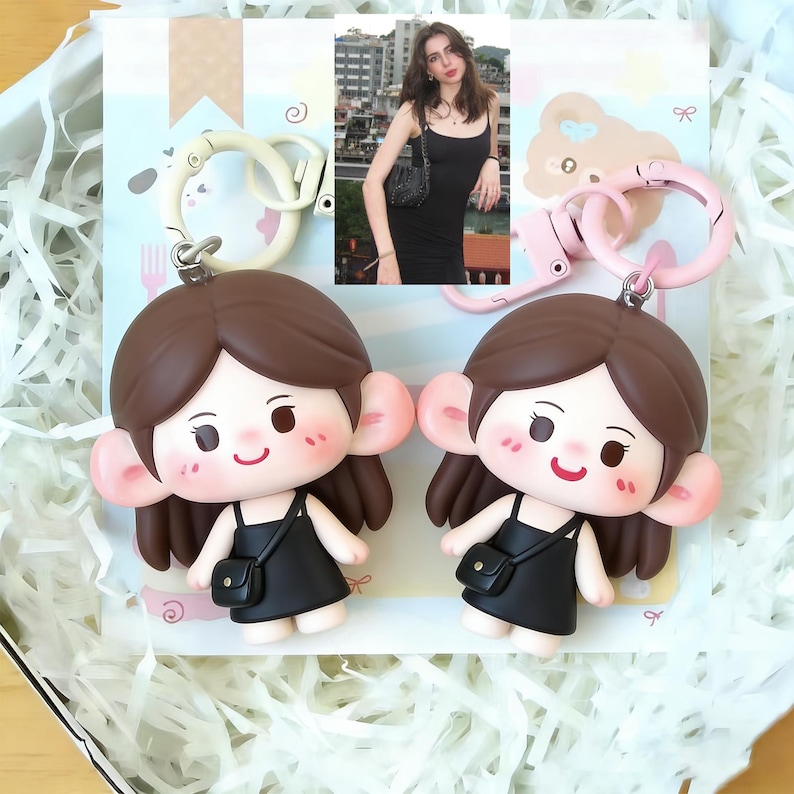 May include: Two keychains featuring a cartoon girl with brown hair, large ears, and a black dress. Each keychain has a matching color ring. The background includes a photo of a woman in a black dress.