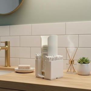 May include: A white bathroom organizer with compartments for cotton swabs, cups, and a tall cylindrical container. The organizer sits on a wooden countertop, with a gold faucet and a small succulent in a white pot in the background.