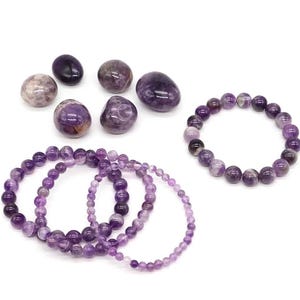 May include: An assortment of amethyst gemstones and bracelets. The gemstones vary in size and shape, displaying shades of purple and lavender. Several beaded bracelets are also visible, showcasing the same color palette, perfect for jewelry making or crystal healing.