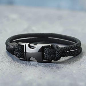 Puede incluir: Pulsera de cuerda negra con cierre de acero inoxidable. La pulsera presenta un dise&ntilde;o de doble hebra con una textura tejida. El cierre es rectangular con una abertura curva. Circunferencia aproximada de 20 cm.