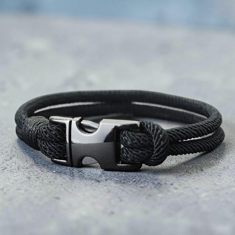 Puede incluir: Pulsera de cuerda negra con cierre de acero inoxidable. La pulsera presenta un dise&ntilde;o de doble hebra con una textura tejida. El cierre es rectangular con una abertura curva. Circunferencia aproximada de 20 cm.