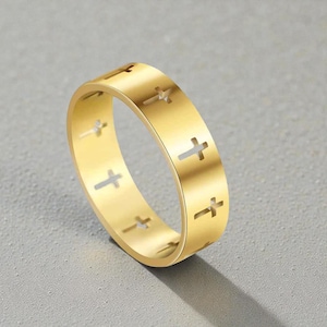 May include: A gold-colored ring with a series of cross cutouts. The ring is made of a shiny, metallic material and has a smooth surface. The ring is a religious-themed accessory.