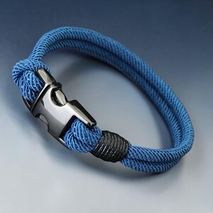 Puede incluir: Una pulsera de cuerda azul con un cierre plateado. La pulsera est&aacute; hecha de dos hebras de cuerda azul, aseguradas con una secci&oacute;n envuelta en negro. El cierre es de color met&aacute;lico brillante.