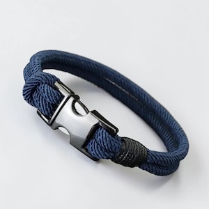 Puede incluir: Una pulsera de cuerda azul marino con un cierre plateado. La pulsera est&aacute; hecha de una cuerda gruesa y trenzada. El cierre es de forma rectangular con un cierre seguro. Un acento negro est&aacute; cerca del cierre. Circunferencia de unos 20 cm.