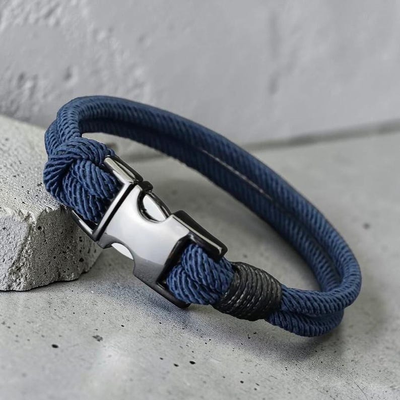 Puede incluir: Una pulsera azul marino con un cierre plateado. La pulsera est&aacute; hecha de cuerda trenzada. El cierre es de forma rectangular. Un accesorio elegante.