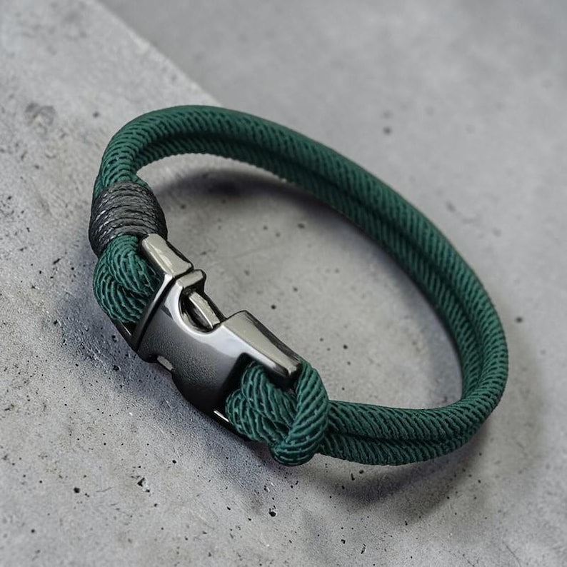 Puede incluir: Una pulsera de cuerda verde con un cierre de metal de ca&ntilde;&oacute;n de fusil. La pulsera est&aacute; hecha de dos hebras de cuerda verde, anudadas en un extremo. El cierre tiene forma rectangular con un cierre seguro.