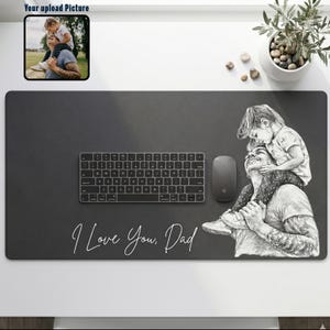 May include: A black desk mat with a keyboard, mouse, and a pencil sketch of a person carrying a child on their shoulders. The text "I Love You, Dad" is written in white cursive. A small framed picture is in the upper left corner.