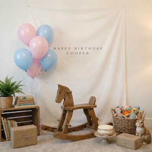 May include: A birthday scene with pink and blue balloons, a wooden rocking horse, and a small cake. The backdrop features the text "HAPPY BIRTHDAY COOPER". Other elements include a wicker basket with toys, a decorative rabbit, and wrapped gifts.