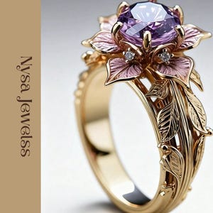 Könnte beinhalten: Ein goldfarbener Ring mit einem großen, runden, lila Edelstein in der Mitte, umgeben von rosa und goldenen floralen Details. Das Band des Rings ist mit blattartigen Gravuren verziert. Der Text "Nysa Jewelss" befindet sich auf der linken Seite.