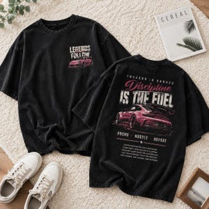 May include: Two black t-shirts with car graphics and text. One shirt reads "LEGENDS FOLLOW" with a pink car graphic. The other shirt says "SUCCESS IS EARNED Discipline IS THE FUEL" with a pink car graphic and the words "FOCUS - HUSTLE - REPEAT".