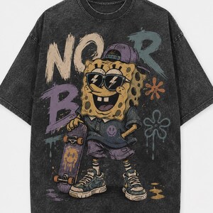 Puede incluir: Una camiseta gris carb&oacute;n con efecto lavado al &aacute;cido que presenta un gr&aacute;fico de un personaje de esponja amarillo con gorra morada y gafas de sol, sosteniendo un monopat&iacute;n. El dise&ntilde;o incluye el texto "NO R" y "B" en estilo grafiti.