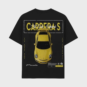 Puede incluir: Camiseta negra con un gráfico amarillo Porsche Carrera S. El diseño incluye el texto "CARRERA S" y "THE SWEET SPOT" en amarillo. La camiseta tiene cuello redondo clásico y mangas cortas.