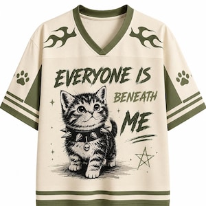 May include: An off-white V-neck jersey with olive green accents, featuring a graphic of a kitten wearing a spiked collar with a skull charm. The text "EVERYONE IS BENEATH ME" is printed above the kitten, accompanied by flame, paw print, and star motifs.