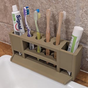 May include: A beige toothbrush holder with multiple slots for toothbrushes and toothpaste. The holder contains several toothbrushes with different colored bristles and two tubes of toothpaste, one labeled "Signal".