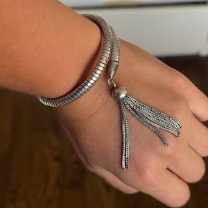 May include: A silver-toned wrap bracelet featuring a flexible, segmented snake-like chain design. The bracelet terminates in a polished metal bead that supports a dangling tassel composed of multiple fine, delicate silver-toned chain strands.