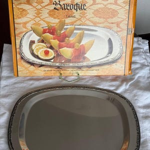 Peut inclure: Un plateau de service ovale argenté avec une bordure décorative. Le plateau est présenté avec une boîte qui indique "Baroque Tablett" et présente un motif floral. Le plateau est adapté pour servir des aliments.