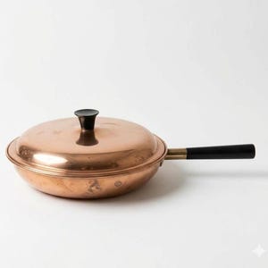 May include: A round copper pan with a matching lid and a long black handle. The pan features a polished metallic finish, a central black knob on the lid, and a brass-colored connector between the pan body and the black handle.