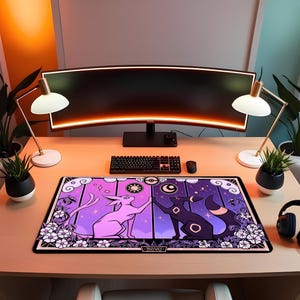 May include: A rectangular desk mat featuring a purple and black design with two stylized cat-like creatures. The mat has a black border and white floral accents. A keyboard, mouse, and monitor are visible on the desk.
