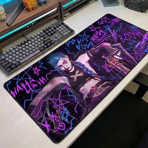 May include: A black rectangular mousepad featuring a graphic of a character with blue hair and a weapon, with the words "POW POW", "BOOM", and "HAHA" in neon colors. The mousepad is on a white desk next to a black keyboard.