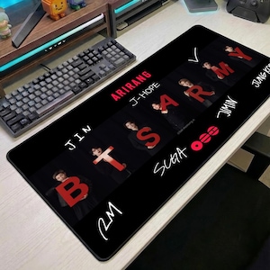 Könnte beinhalten: Schwarzes rechteckiges Mauspad mit den roten Buchstaben "BTS", dem Wort "ARMY" und den Namen der Bandmitglieder. Das Mauspad hat einen schwarzen Hintergrund und liegt auf einem weißen Schreibtisch neben einer schwarzen Tastatur.