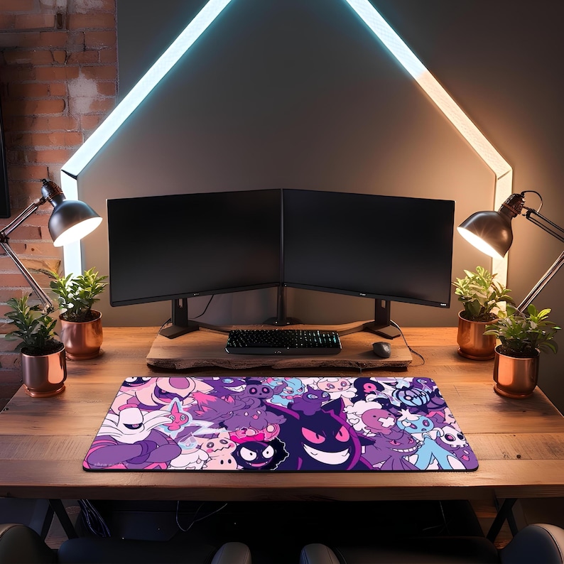 May include: A rectangular mouse mat with a vibrant design of cartoon characters in purple, pink, and blue. The mat sits on a wooden desk, with two computer monitors, a keyboard, and desk lamps in the background. The desk is made of wood.
