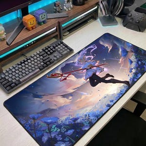 Może przedstawiać: Prostokątna podkładka pod mysz do gier z fantastyczną ilustracją w stylu anime. Grafika przedstawia postać w niebiesko-białym stroju, dzierżącą laskę, na tle zachmurzonego nieba i niebieskich kwiatów.