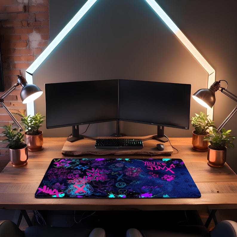 May include: A rectangular gaming mousepad with a vibrant design featuring neon pink and blue graphics on a dark blue background. The mousepad is placed on a wooden desk, with a keyboard, mouse, and dual monitors in the background.