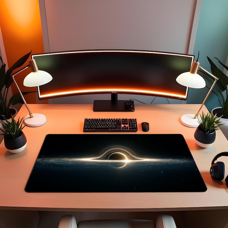 May include: A black desk mat with a luminous black hole design. The mat is rectangular and placed on a light wooden desk. A curved monitor, keyboard, mouse, and desk lamps are also visible.