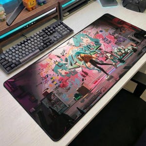 May include: A rectangular desk mat featuring a vibrant, graffiti-style illustration of a teal-haired anime character. The design includes pink and purple paint splatters, stylized text, and urban street art elements across a dark, textured background.