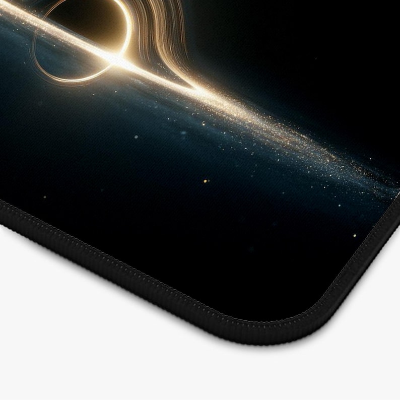 May include: A black mousepad with a detailed illustration of a black hole, highlighted by golden light and cosmic features. The design presents a celestial scene with a dark blue and black backdrop, and a black stitched edge.