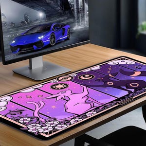 May include: A rectangular desk mat featuring a vibrant design with a pink and purple color scheme. The mat showcases stylized illustrations of creatures, stars, and floral elements. A computer monitor displaying a blue sports car is in the background.