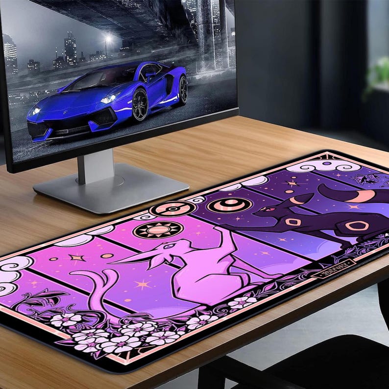 May include: A rectangular desk mat featuring a vibrant design with a pink and purple color scheme. The mat showcases stylized illustrations of creatures, stars, and floral elements. A computer monitor displaying a blue sports car is in the background.