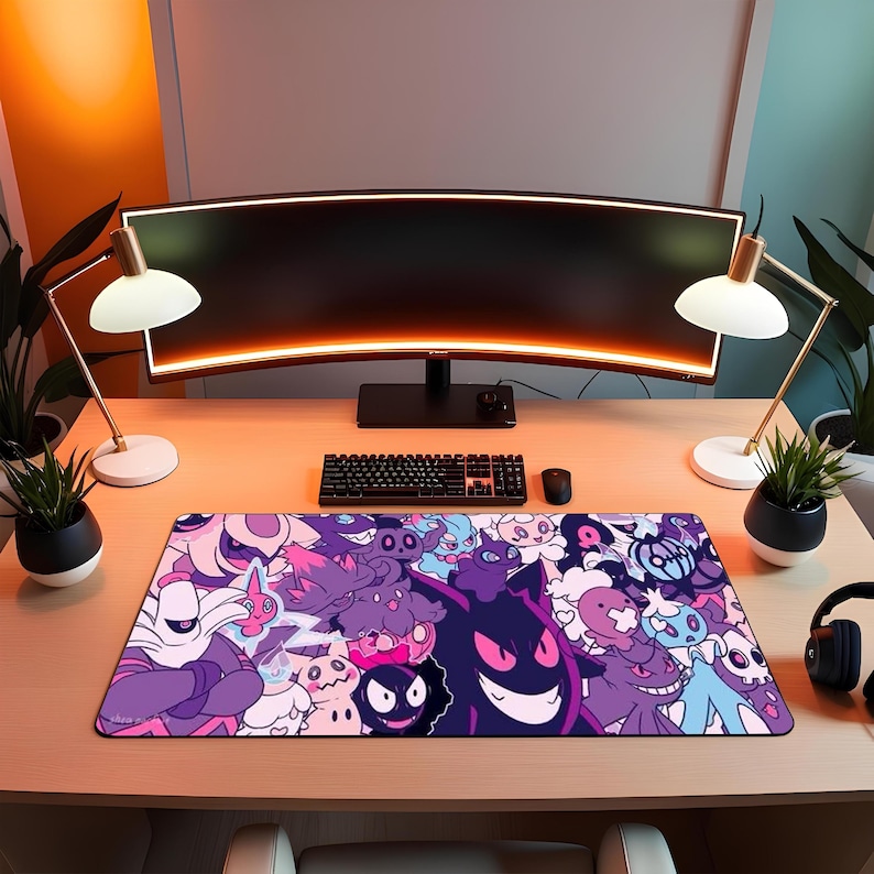 May include: A rectangular desk mat with a cartoon design in purple, pink, and blue. The mat is on a wooden desk, with a computer monitor, keyboard, and mouse behind it. The desk also has two lamps and small potted plants.