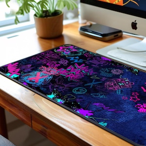 May include: A rectangular mousepad with a dark blue denim-like background. The surface is covered in neon graffiti-style art in shades of pink, purple, teal, and blue. The design includes various symbols and text elements.
