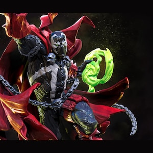 May include: A detailed action figure of Spawn, a comic book character, with a black and white costume, red cape, and chains. The figure is holding a glowing green energy effect. The logo "nom nom Figures" is in the upper right corner.