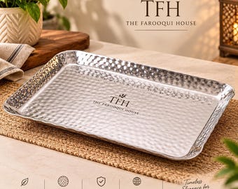 May include: A rectangular silver-toned metal serving tray with a hammered texture finish. The center of the tray features the black printed text TFH THE FAROOQUI HOUSE. The tray has raised edges and a reflective, metallic surface.