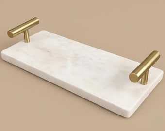 May include: A rectangular white marble serving tray featuring a polished surface with subtle grey veining. The tray is equipped with two cylindrical gold-toned metal handles attached to each of the shorter ends, providing a secure grip for carrying.