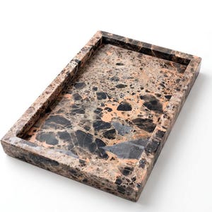 May include: A rectangular tray featuring a polished stone surface with a complex, multi-tonal pattern of black, dark brown, and soft peach-colored fragments. The tray has raised, thick edges and a smooth, glossy finish throughout the entire piece.