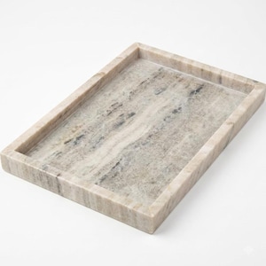 May include: A rectangular tray crafted from natural stone with a polished finish. The surface features a marbled pattern in shades of beige, cream, and soft gray, with distinct veining throughout the material and raised edges on all four sides.