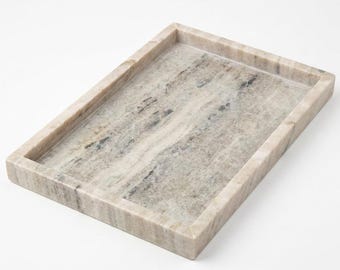 May include: A rectangular tray crafted from natural stone with a polished finish. The surface features a marbled pattern in shades of beige, cream, and soft gray, with distinct veining throughout the material and raised edges on all four sides.