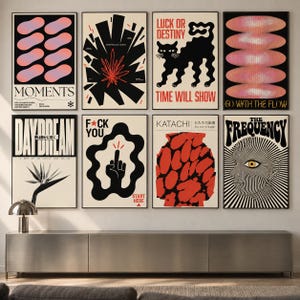 May include: A gallery wall featuring eight framed posters with diverse graphic designs, including abstract shapes, a black cat, a hand gesture, a bird of paradise flower, and a human face, all displayed in a grid arrangement above a long metal console.