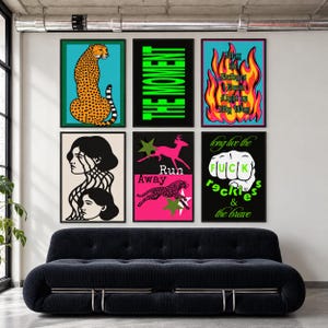 May include: A gallery wall of six framed posters featuring diverse graphic designs: a cheetah on teal, neon green text reading THE MOMENT, flames with text, two faces, a pink panel with a deer and cheetah, and a fist with the text long live the FUCK recklessness & the brave.