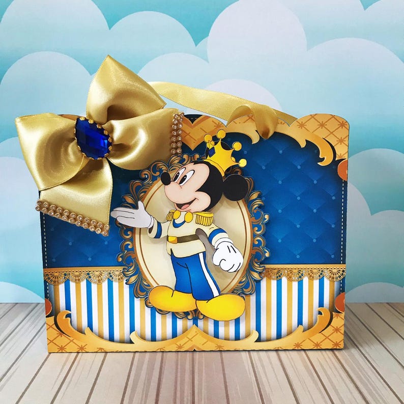 May include: A decorative box featuring a cartoon image of Mickey Mouse in a prince outfit. The box has a blue and gold color scheme, with a large gold bow and a blue jewel. The box has a striped pattern at the bottom.