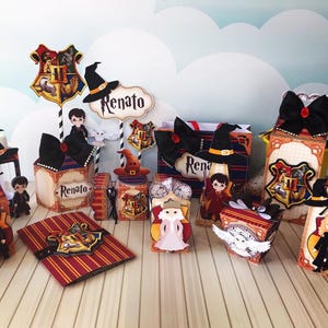 Op de afbeelding: Een verzameling Harry Potter-themafeestdecoraties. De decoraties omvatten dozen, labels en toppers met het Hogwarts-wapen, heksenhoeden en karakterillustraties. Het kleurenschema is voornamelijk rood, goud en zwart.