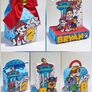 Pode incluir: Uma coleção de caixas de presente e decorações coloridas com o tema Patrulha Pata. As caixas são azuis com pegadas e apresentam recortes de personagens, números e nomes. Uma caixa tem um grande laço vermelho.