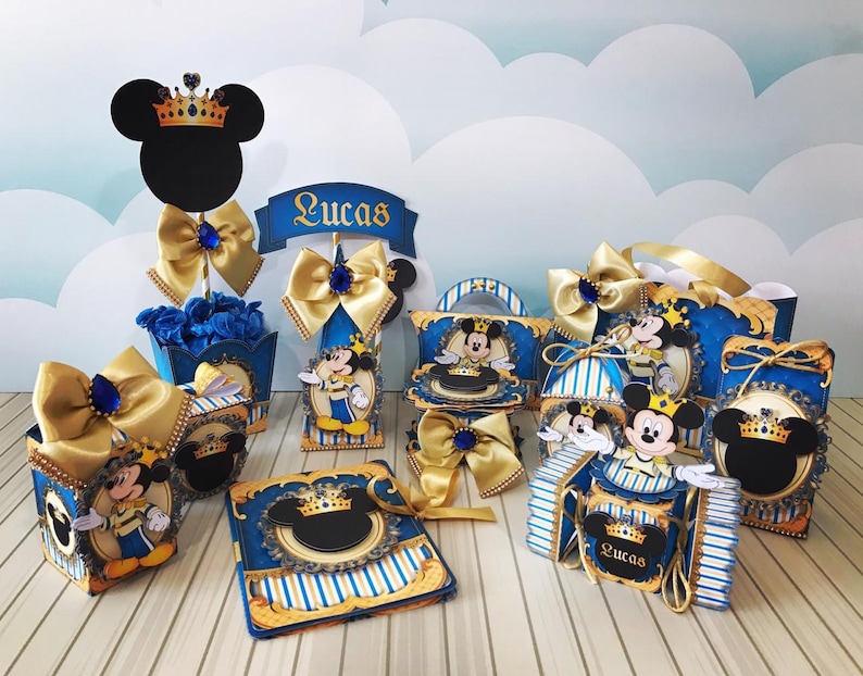May include: A collection of Mickey Mouse-themed party decorations in blue, gold, and white. The decorations include boxes, bows, and cutouts, some with the name "Lucas". The Mickey Mouse silhouette is featured on several items, with a crown.
