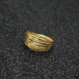Op de afbeelding: Een goudkleurige ring met een getextureerd, gelaagd ontwerp. De ring heeft meerdere banden die een uniek, gestapeld uiterlijk creëren. De ring is gemaakt van een glanzend, metalen materiaal.