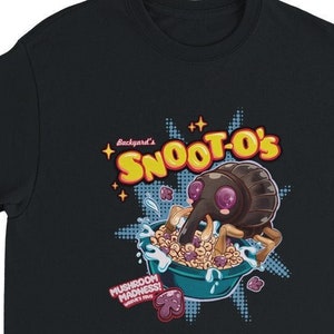 Op de afbeelding: Zwart T-shirt met een cartoonillustratie van een kever die ontbijtgranen eet. De doos met ontbijtgranen zegt "Backyard's Snoot-O's Mushroom Madness!"