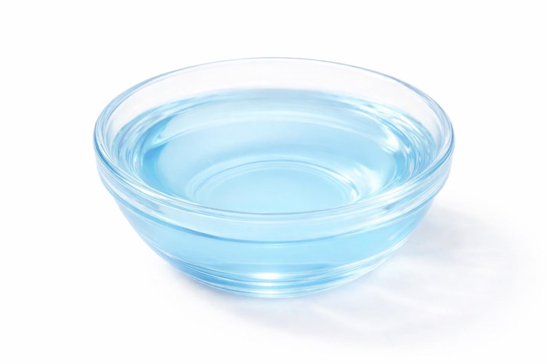 May include: A clear glass bowl filled with a translucent light blue liquid. The bowl features a smooth, rounded design with a thick base and curved sides, containing the liquid which reflects light across its surface against a white background.